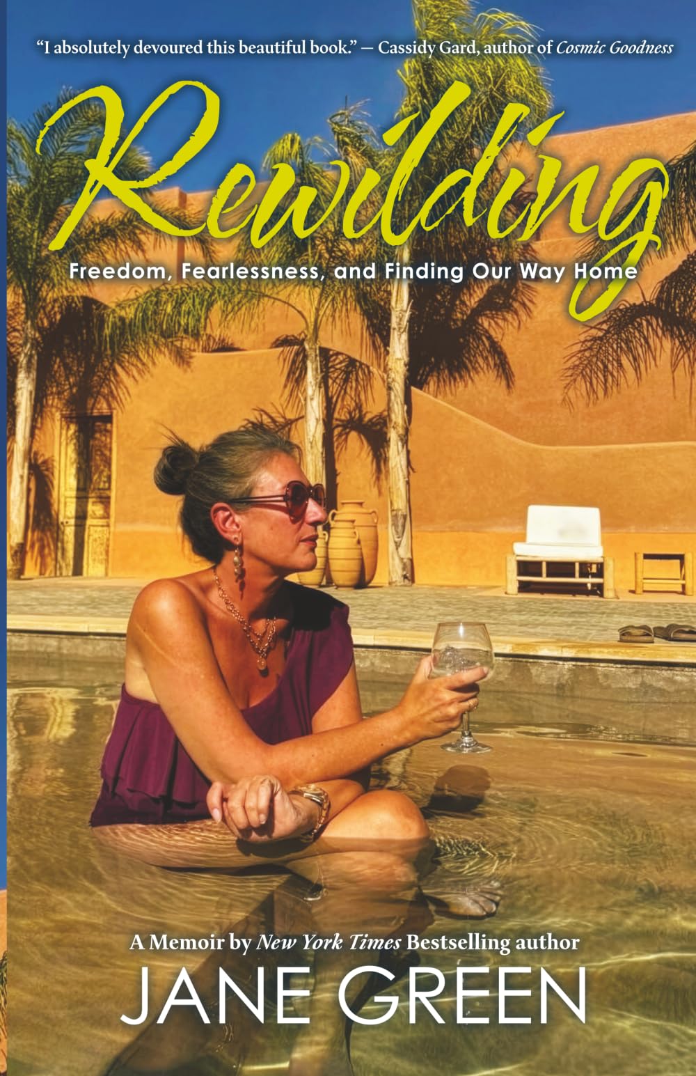 Version 100 – To Speak Online Book cover for 'Rewilding' by Jane Green, showing a woman in a pool with a yellow desert backdrop and palm trees, wearing sunglasses and holding a glass of wine.