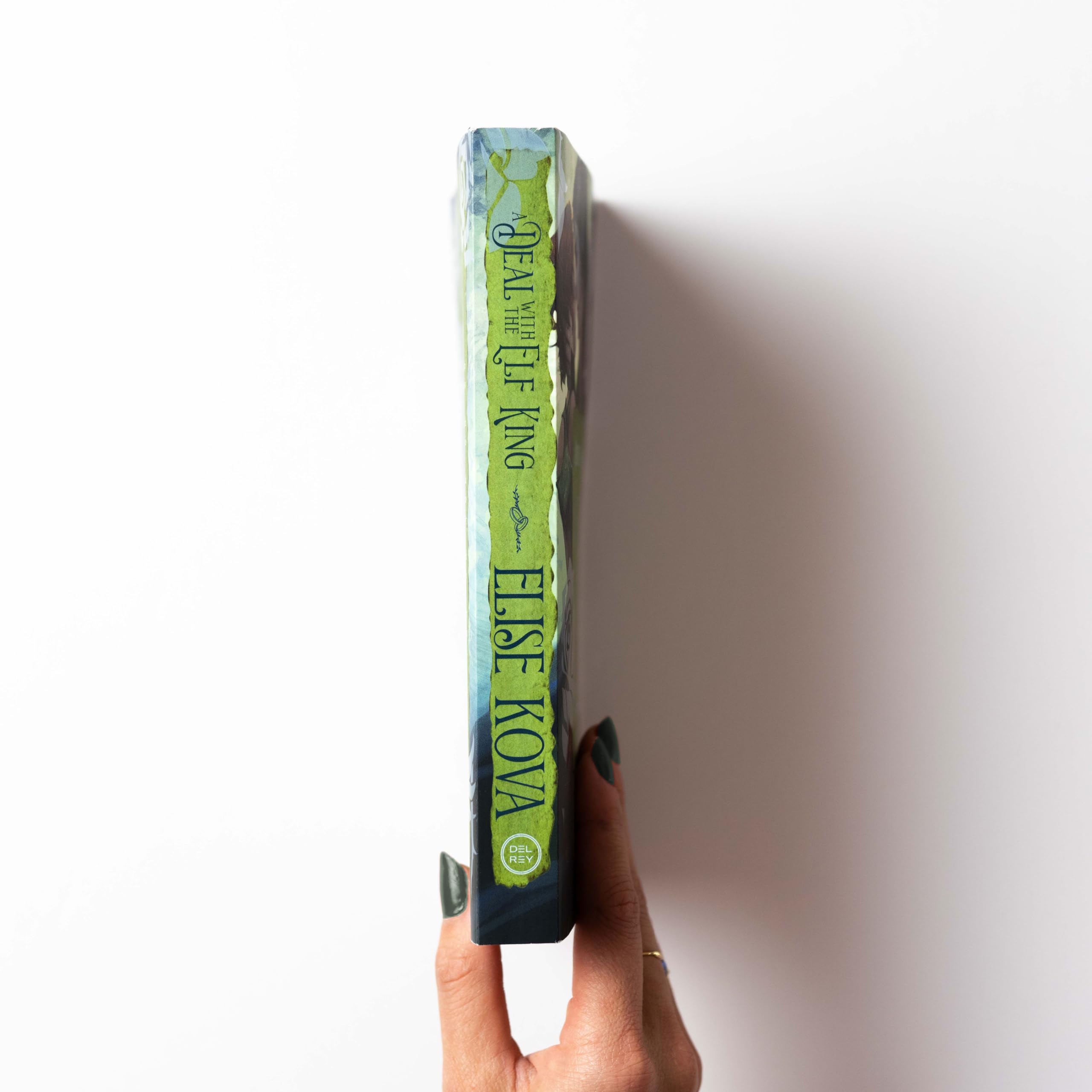 Version 100 – To Speak Online Close-up of a green paperback spine being held upright by fingers, with the publisher name Del Rey visible on the bottom of the spine.