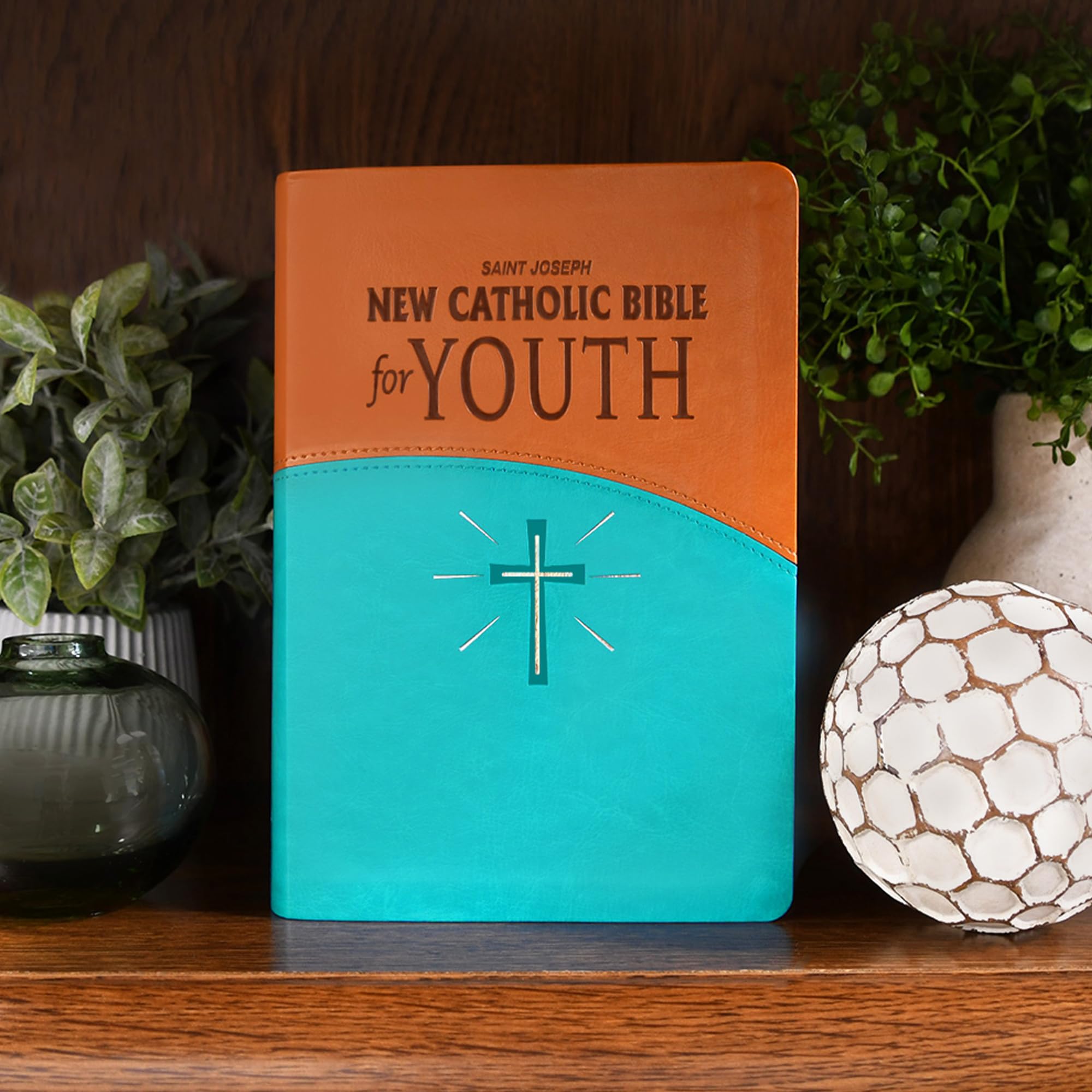 Version 100 – To Speak Online Colored Bible on a shelf: orange cover with turquoise bottom, cross motif, next to greenery and a lattice-patterned ball on the right